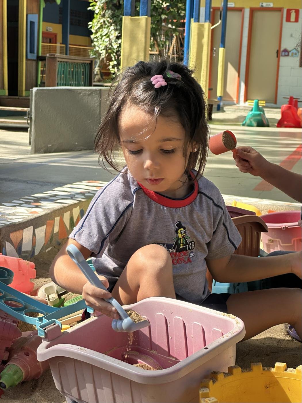 Menina brincando com peneira e potes na areia