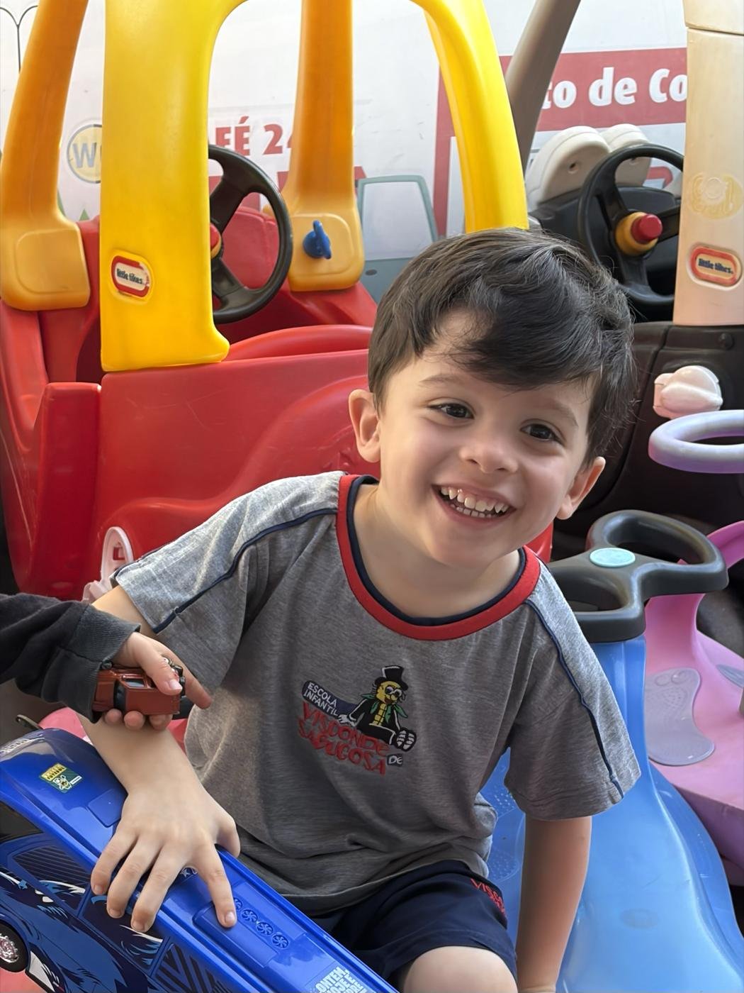 Menino sorrindo dentro de um carrinho de brinquedo no pátio da escola